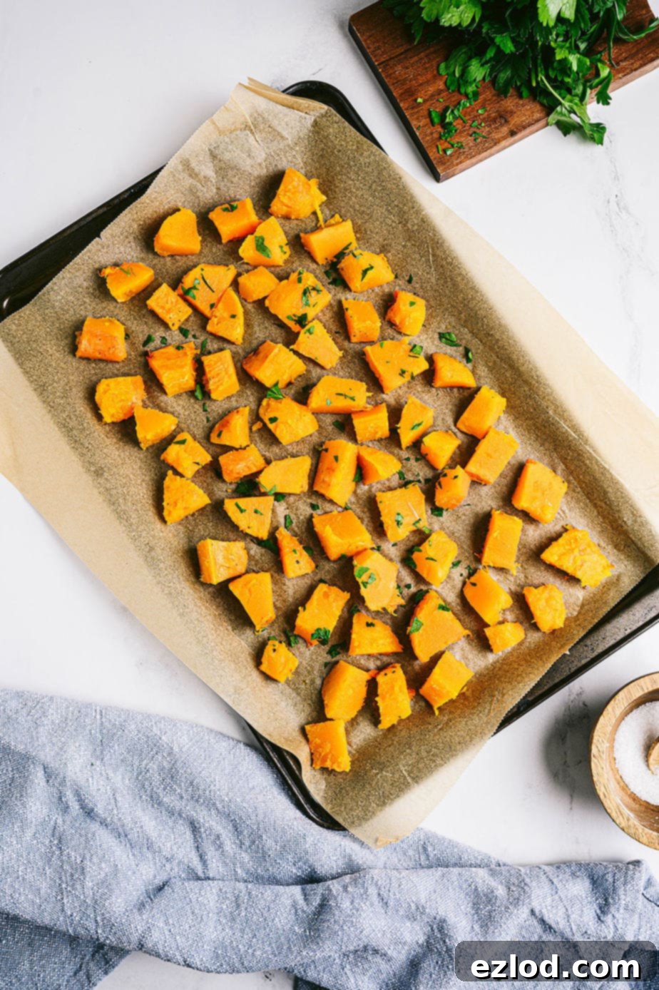 Overhead photo of cooked and cubed butternut squash on a parchment-lined baking sheet, showcasing its golden-brown edges.