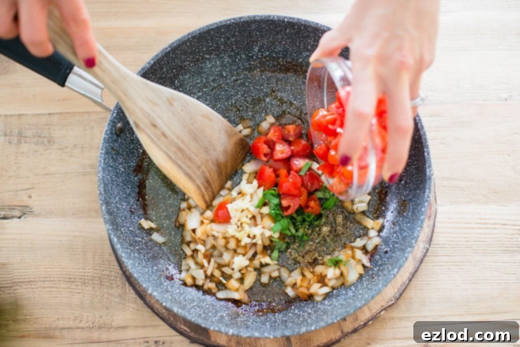 A woman is mixing tomatoes, garlic, onions, and basil in a pan on a wooden table. 