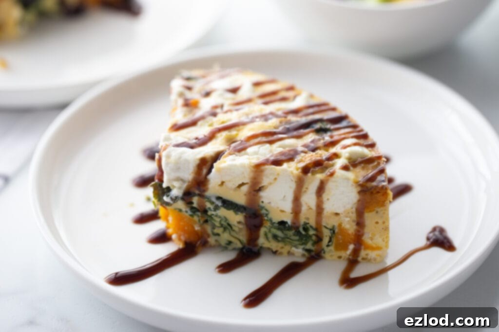 A close-up, landscape photo of a slice of fluffy frittata, beautifully topped with creamy goat cheese crumbles and a delicate drizzle of balsamic glaze.