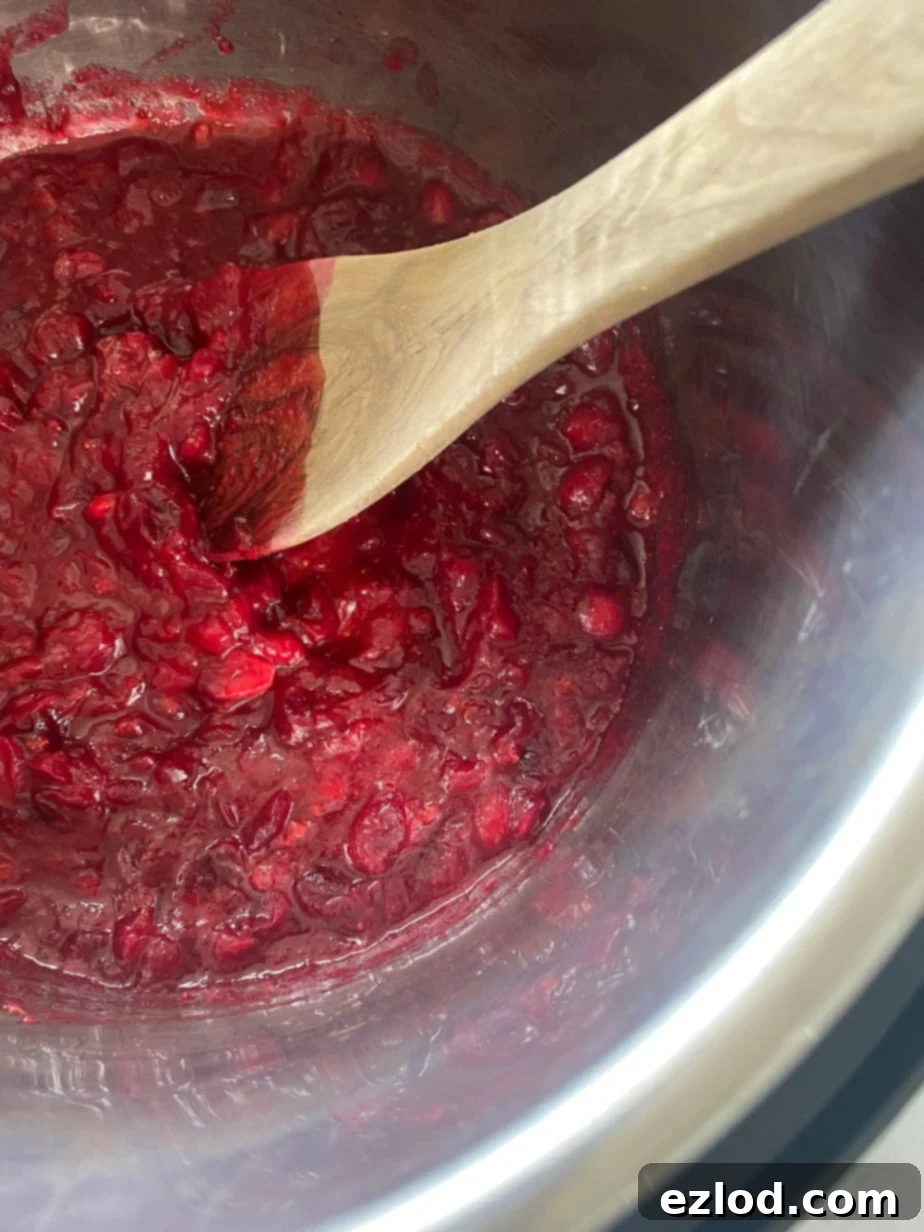 Cooked cranberry sauce in an Instant Pot liner with a wooden spoon.