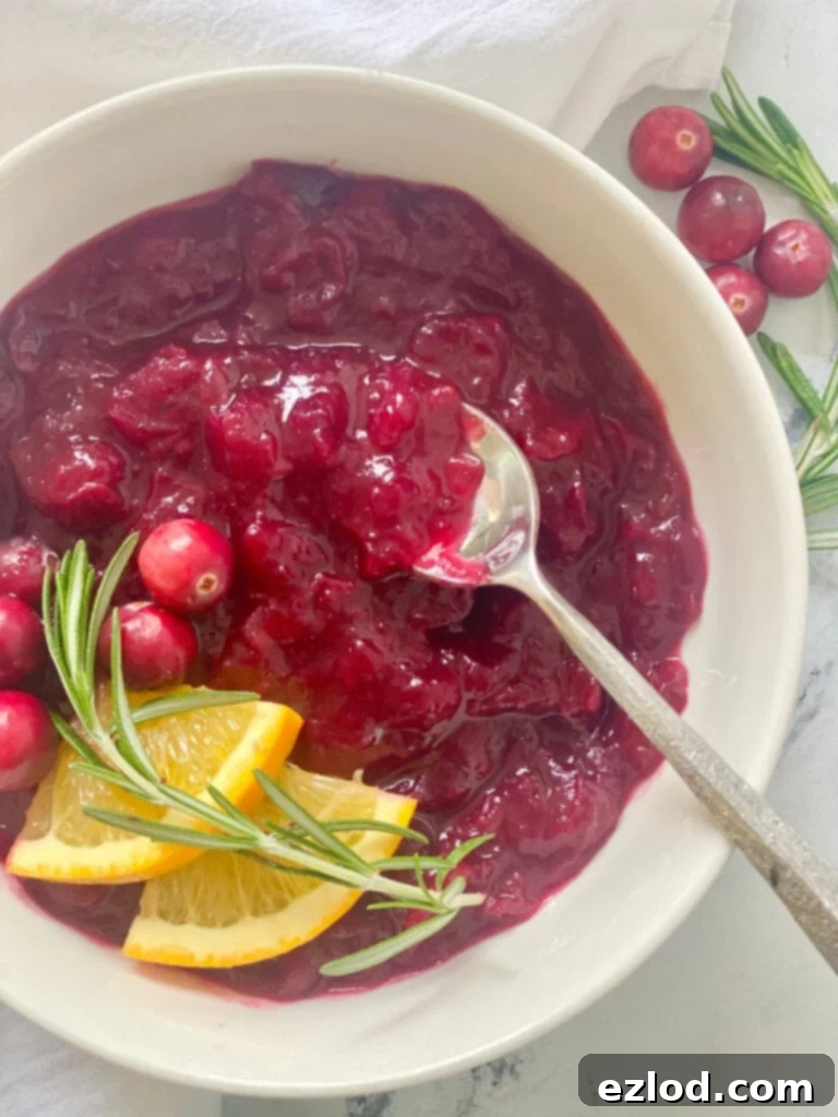 Close up photo: cranberry sauce in a bowl with orange, cranberries, and rosemary as garnish.