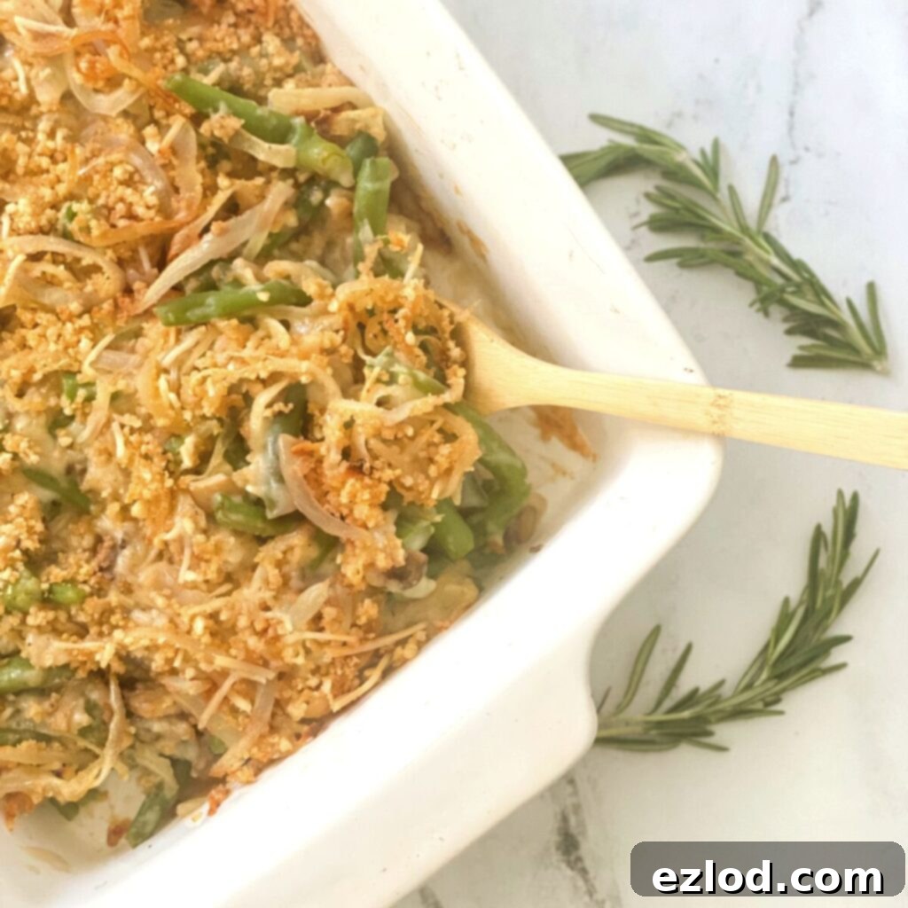 Wholesome Gluten Free Green Bean Casserole 2 Overhead image: a beautiful healthy green bean casserole with golden crispy onion topping in a white casserole dish, with a wooden spoon for serving.