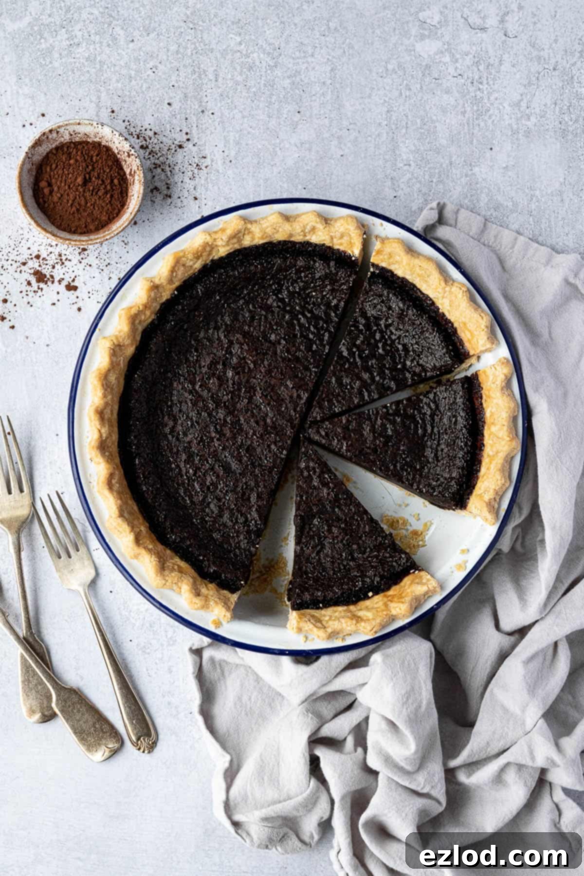 A stunning vegan chocolate chess pie, nestled in an enamel pie dish, surrounded by forks and a small bowl of rich cocoa powder. The perfect festive dessert.