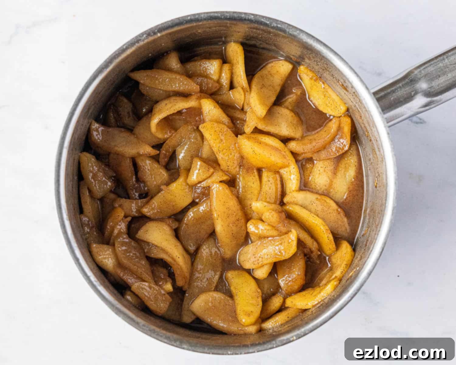 Step-by-step image showing the cooked apple filling in a pan, glistening with syrup, ready for the next stage of the recipe.