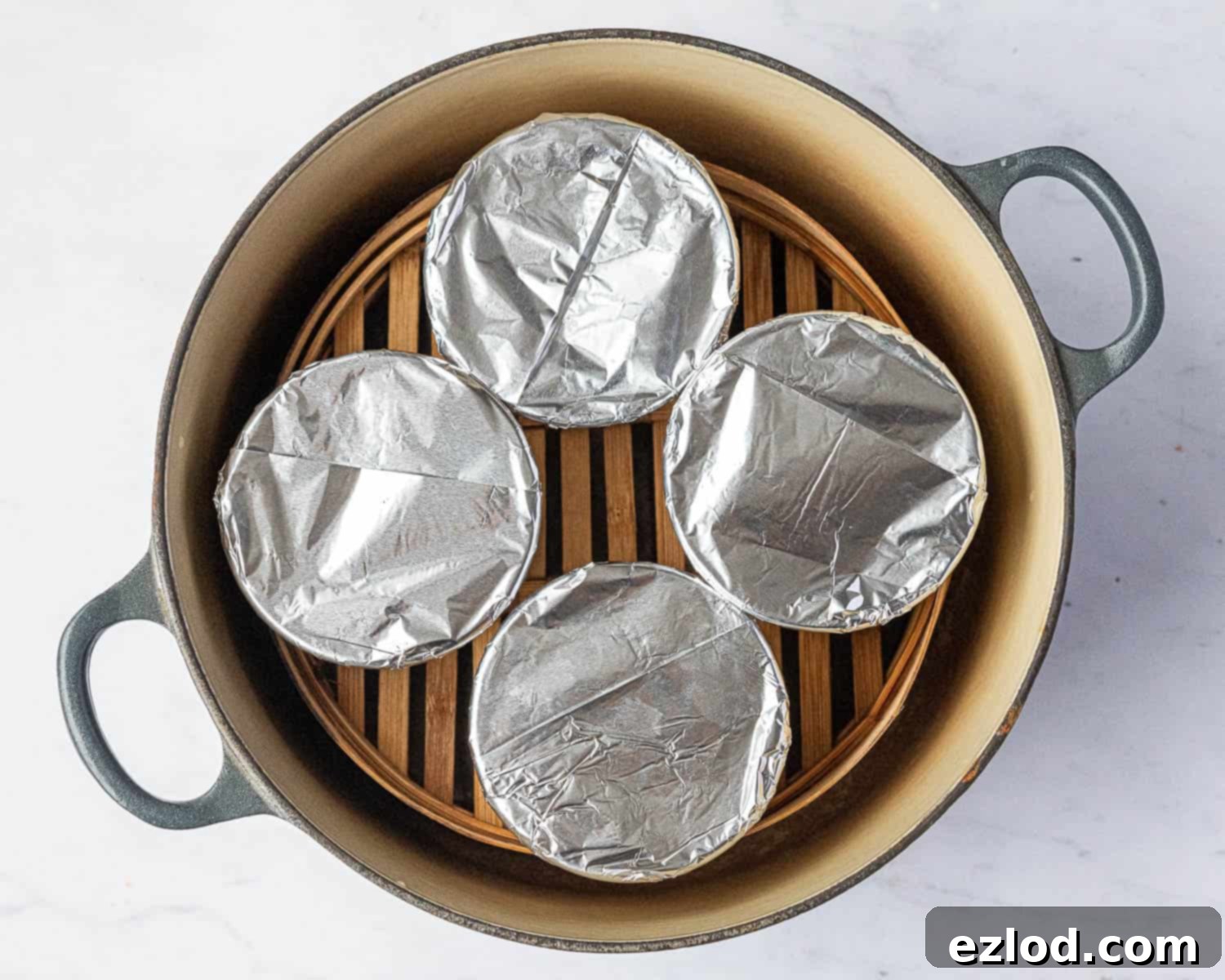 Individual pudding bowls steaming in a pot, covered with a lid.