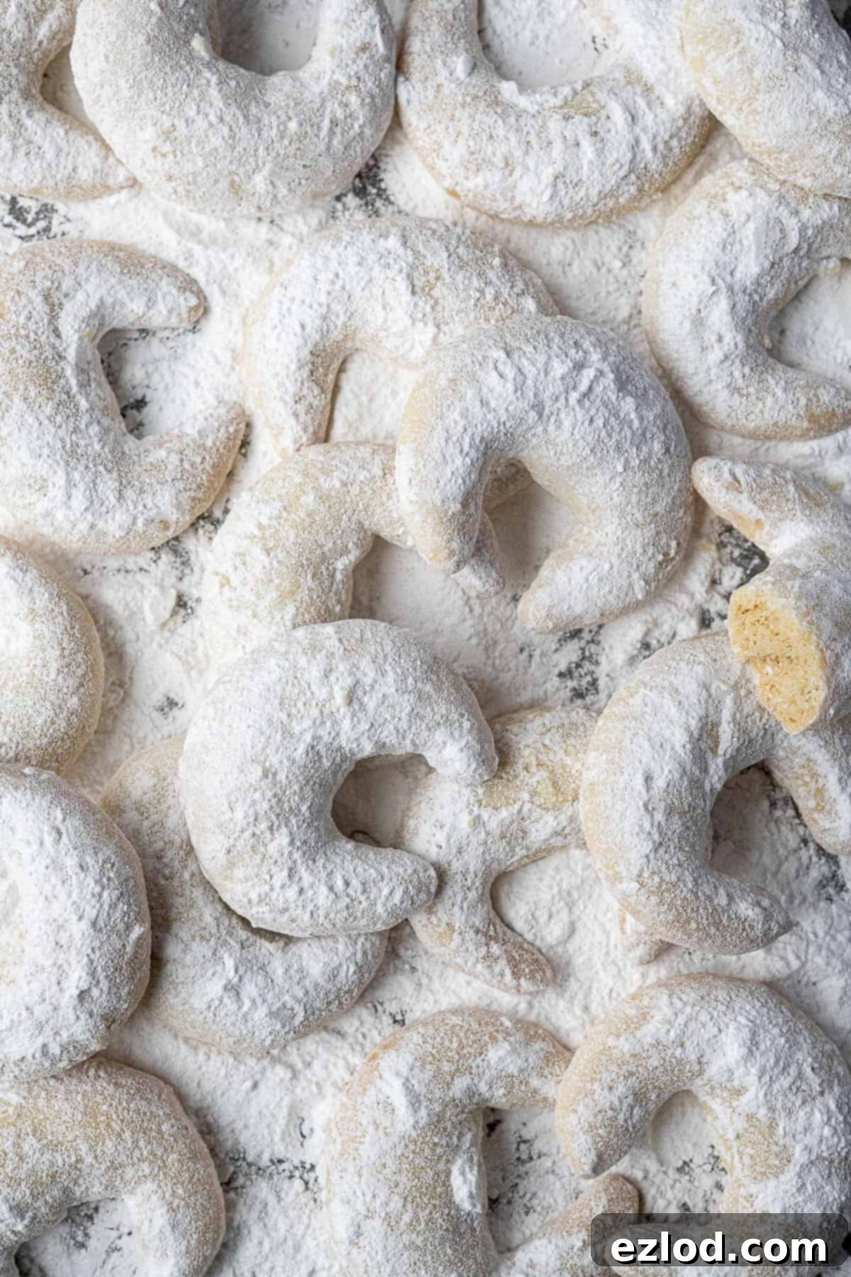 Freshly baked Vegan Vanillekipferl, dusted with icing sugar, arranged artfully on a light surface.