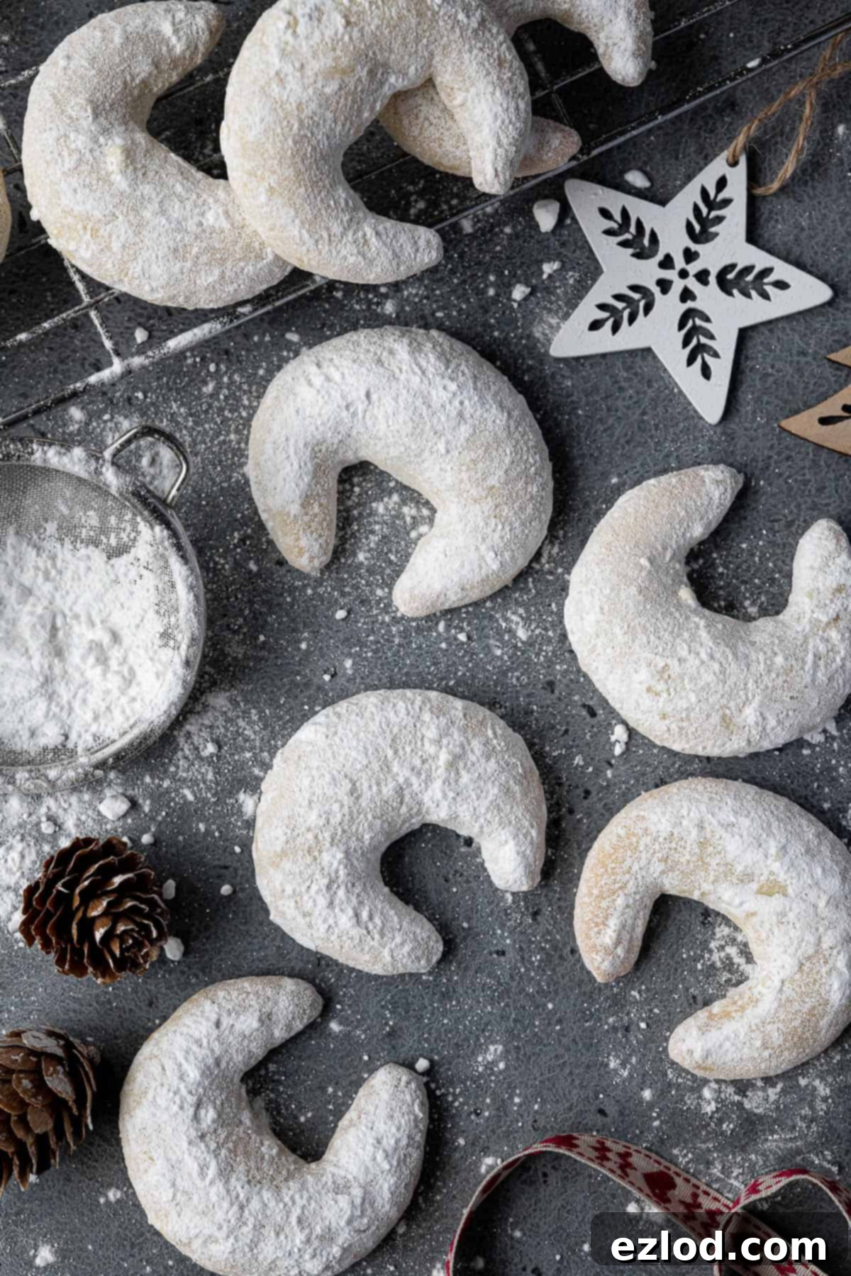 A beautifully composed flat lay image showcasing Vegan Vanillekipferl on a grey surface, surrounded by festive pine cones and Christmas ornaments.