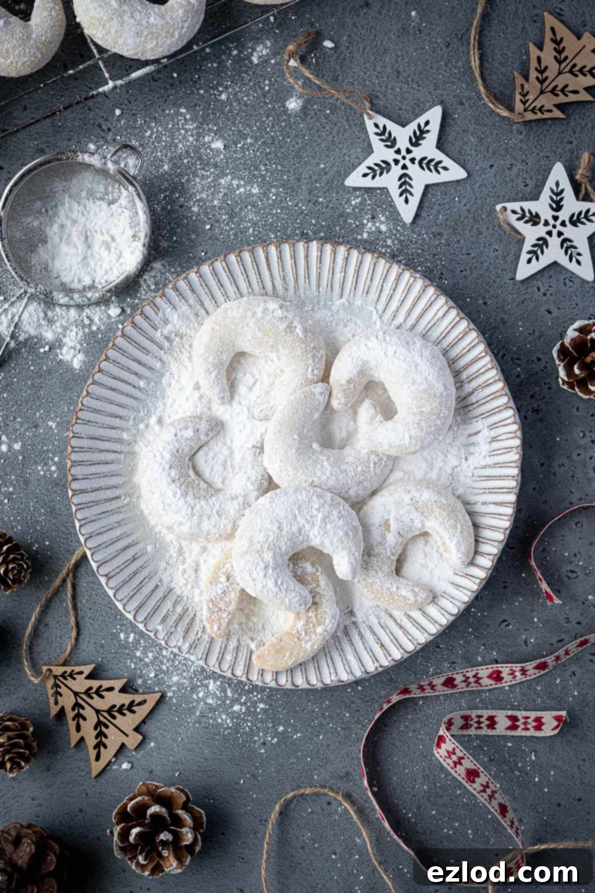 Vegan Vanillekipferl displayed on a white plate, adorned with festive Christmas ornaments and pinecones.