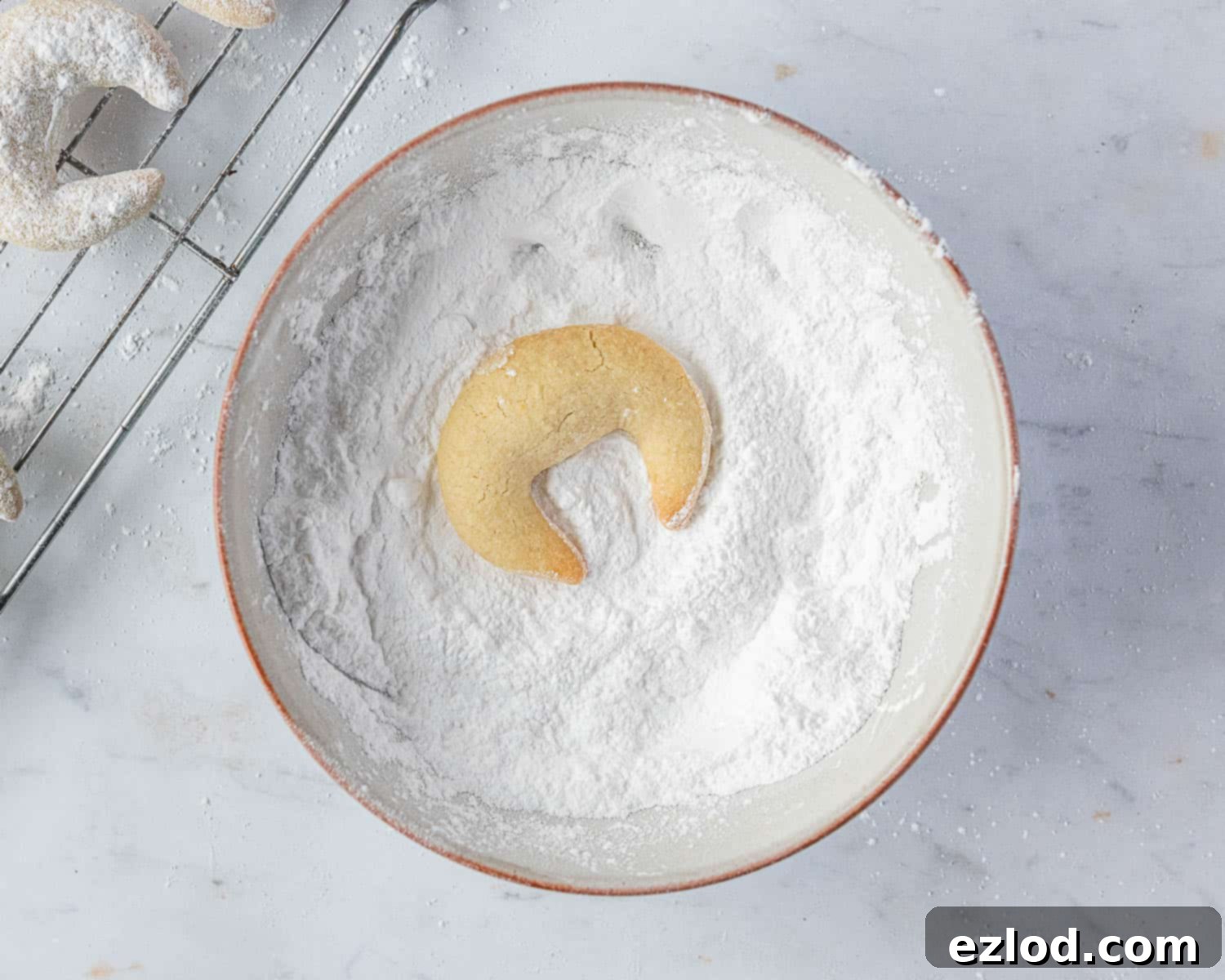 A close-up shot of a hand gently rolling a warm Vanillekipferl in a bowl of icing sugar.