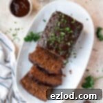 Vegan seitan meatloaf on a plate with bowls of barbecue sauce and pepper.