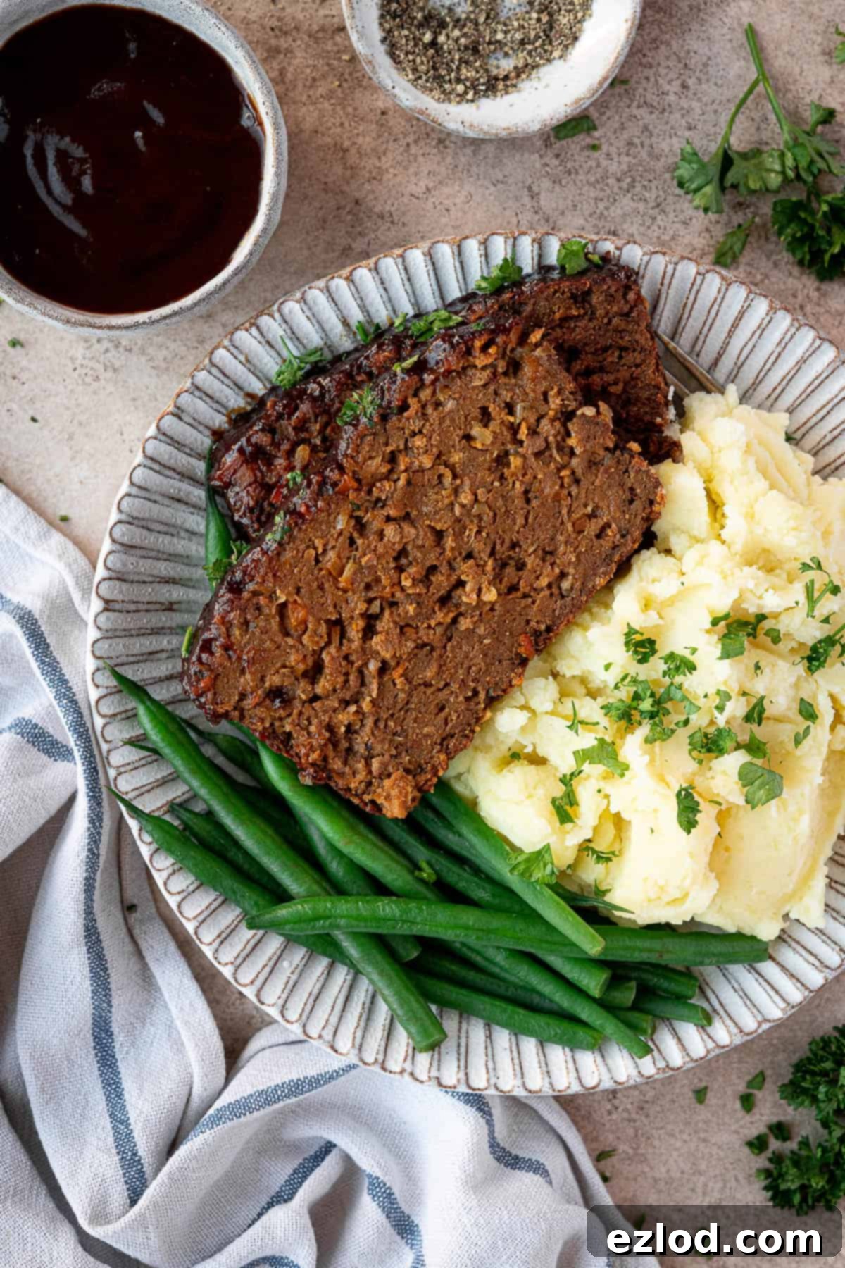 A slice of vegan seitan meatloaf served on a white plate with a side of creamy mashed potato and vibrant green beans.