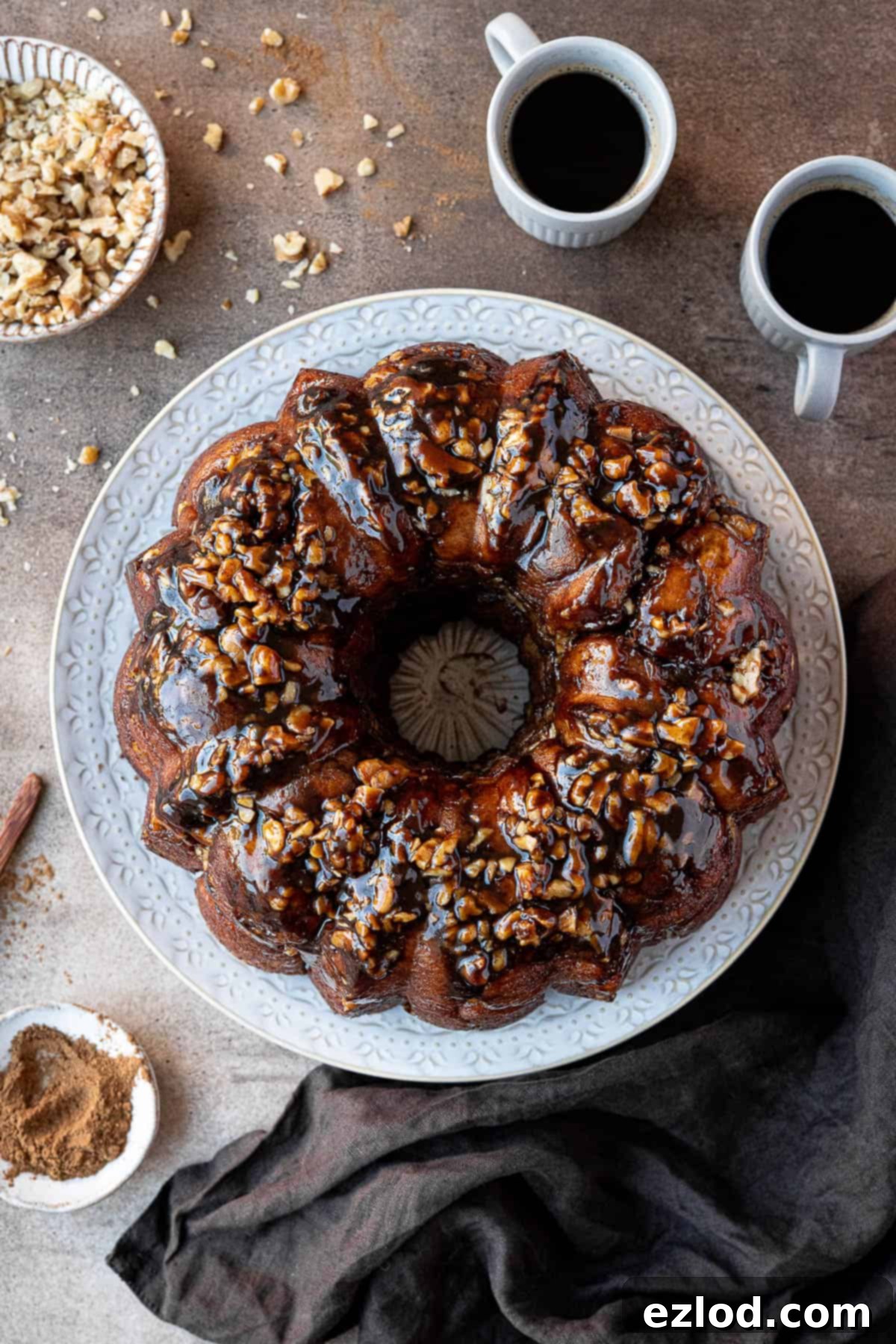Vegan banana monkey bread on a white plate with cups of coffee and bowls of walnuts and cinnamon, illustrating a perfect brunch setup.