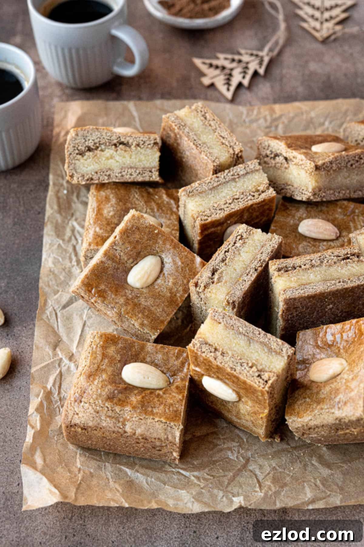Squares of vegan gevulde speculaas on a sheet of baking parchment with two cups of coffee.