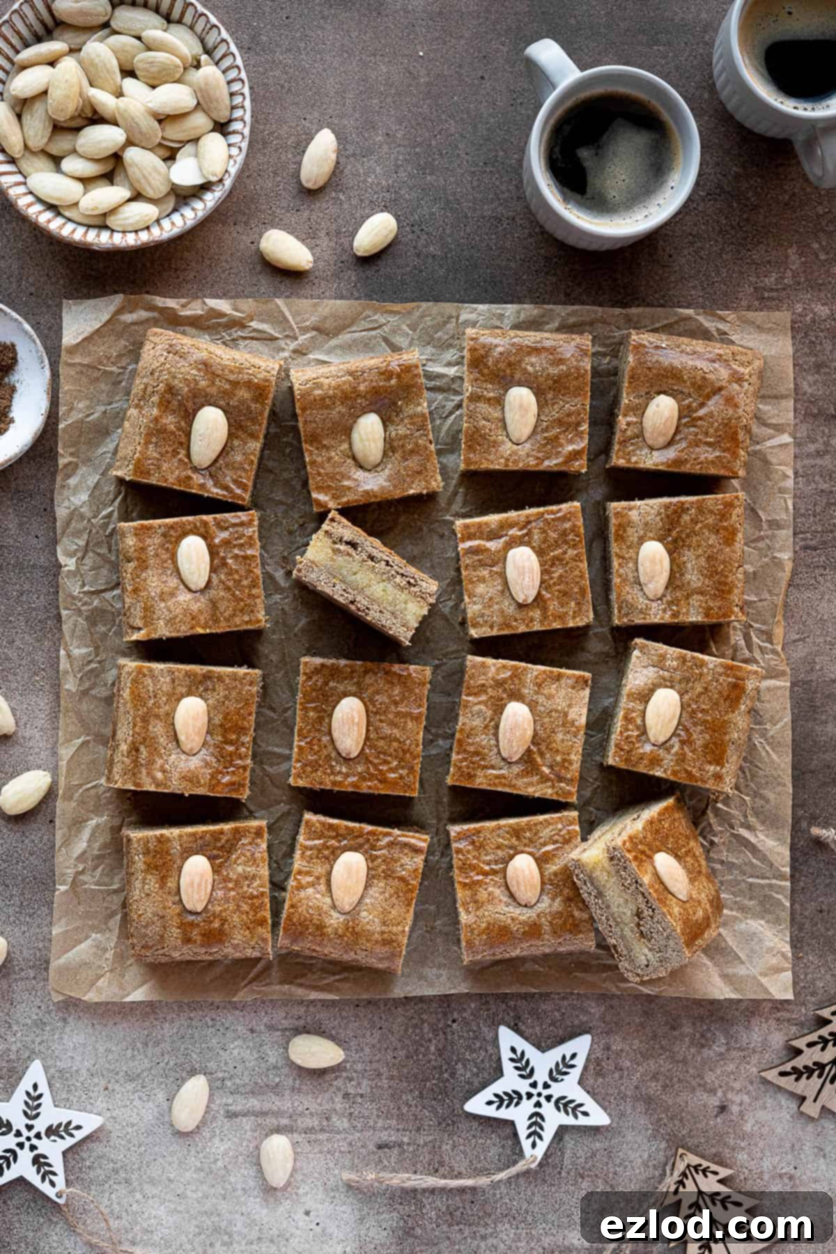 Squares of vegan gevulde speculaas surrounded by cups of coffee, a bowl of almonds and Christmas decorations.