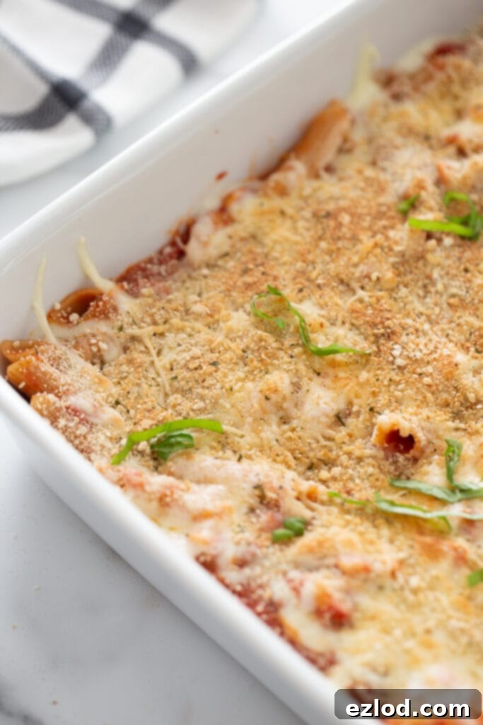 High angle photo of baked chicken parmesan pasta in a white casserole dish, garnished with fresh basil.