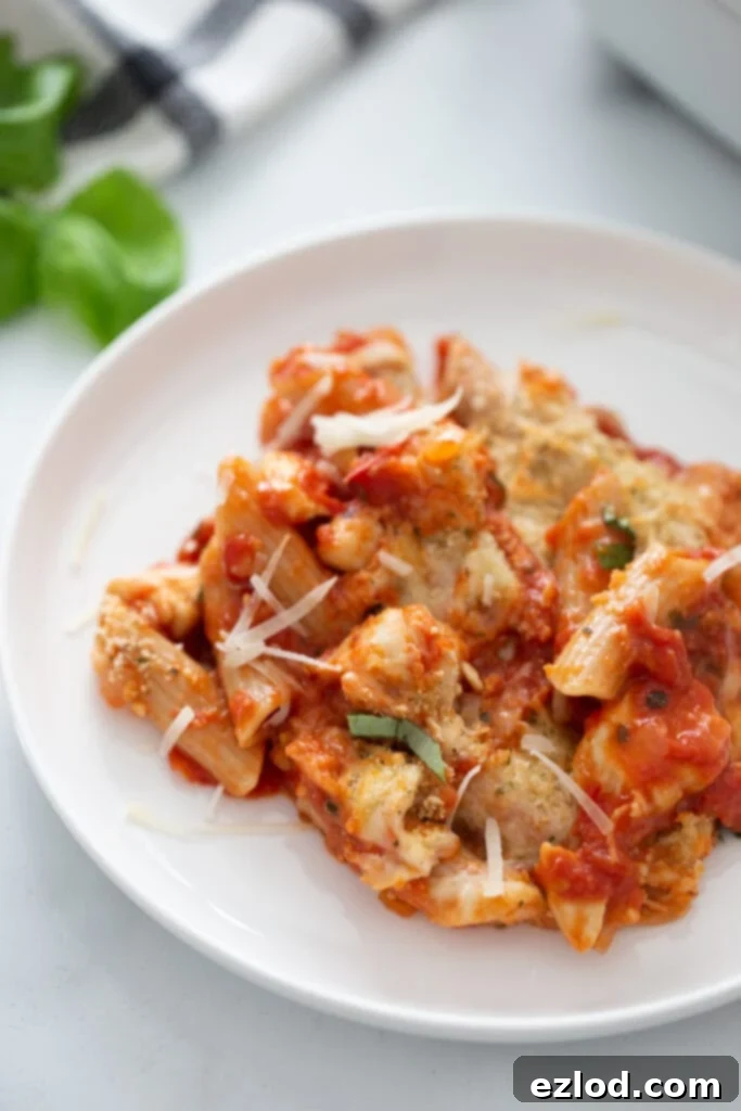 Penne pasta with tomato sauce, shredded cheese, and diced chicken piled high on a white plate.