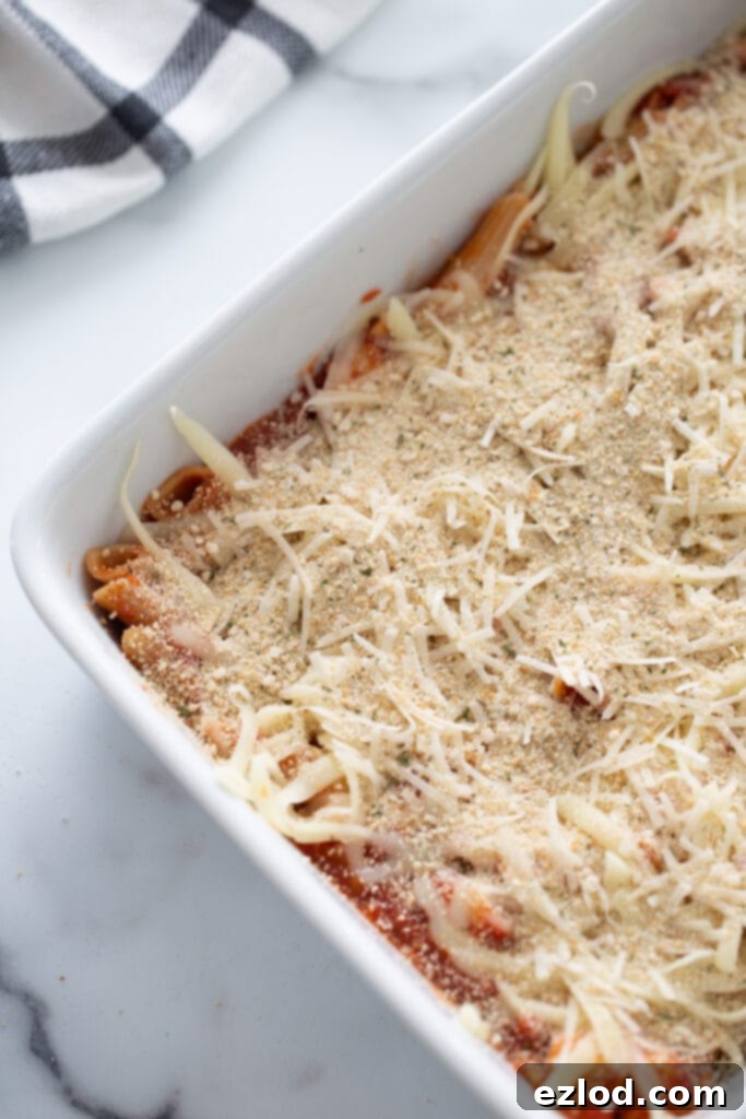 Overhead photo of casserole dish filled with pasta, tomato sauce and shredded cheese, ready for the oven.