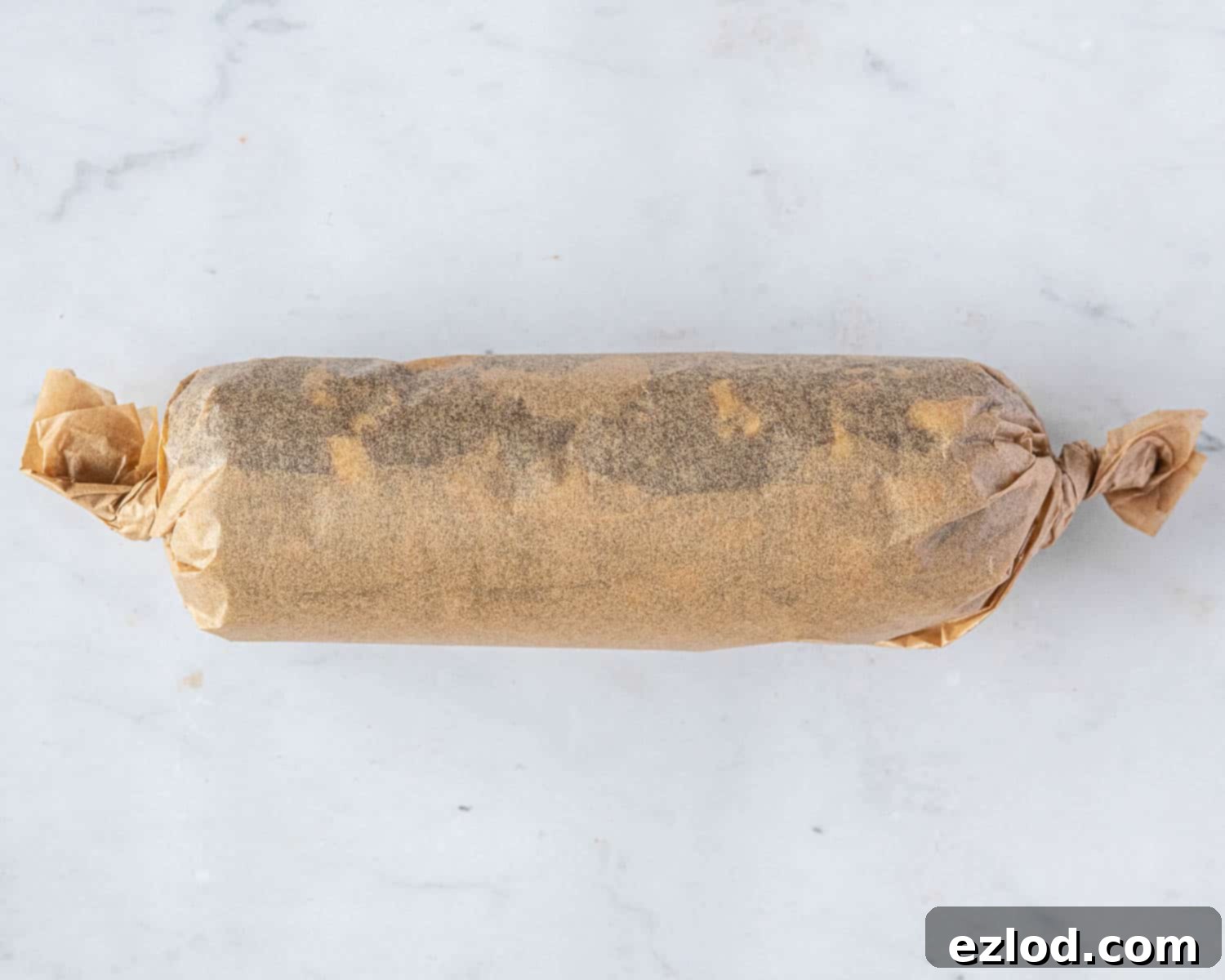 Step 6 in making vegan brunkager: the dough log is tightly wrapped in baking parchment with twisted ends, ready for resting.