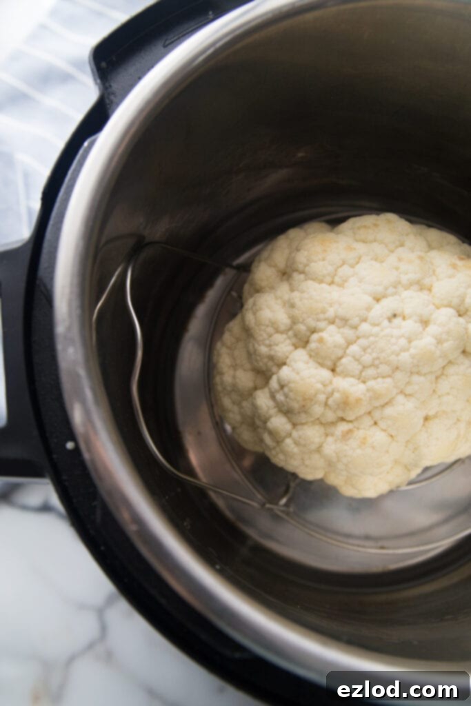 A head of cauliflower placed on a trivet inside an Instant Pot, ready for the 'zero minutes' steaming method for a perfect, tender-crisp texture.