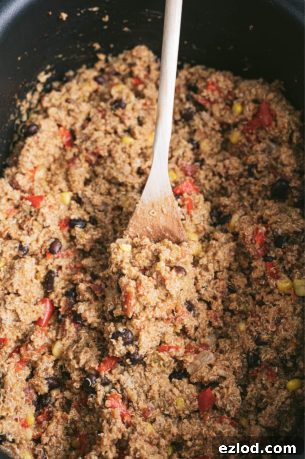 Mexican quinoa casserole in a black crock pot with a wooden spoon.