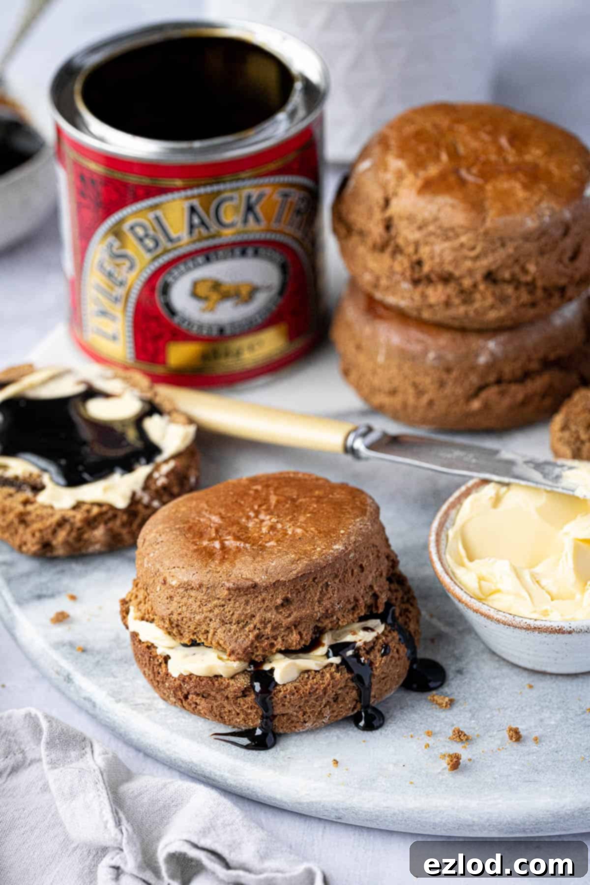 Vegan treacle scones on a marble board with a tin of treacle and a bowl of butter.