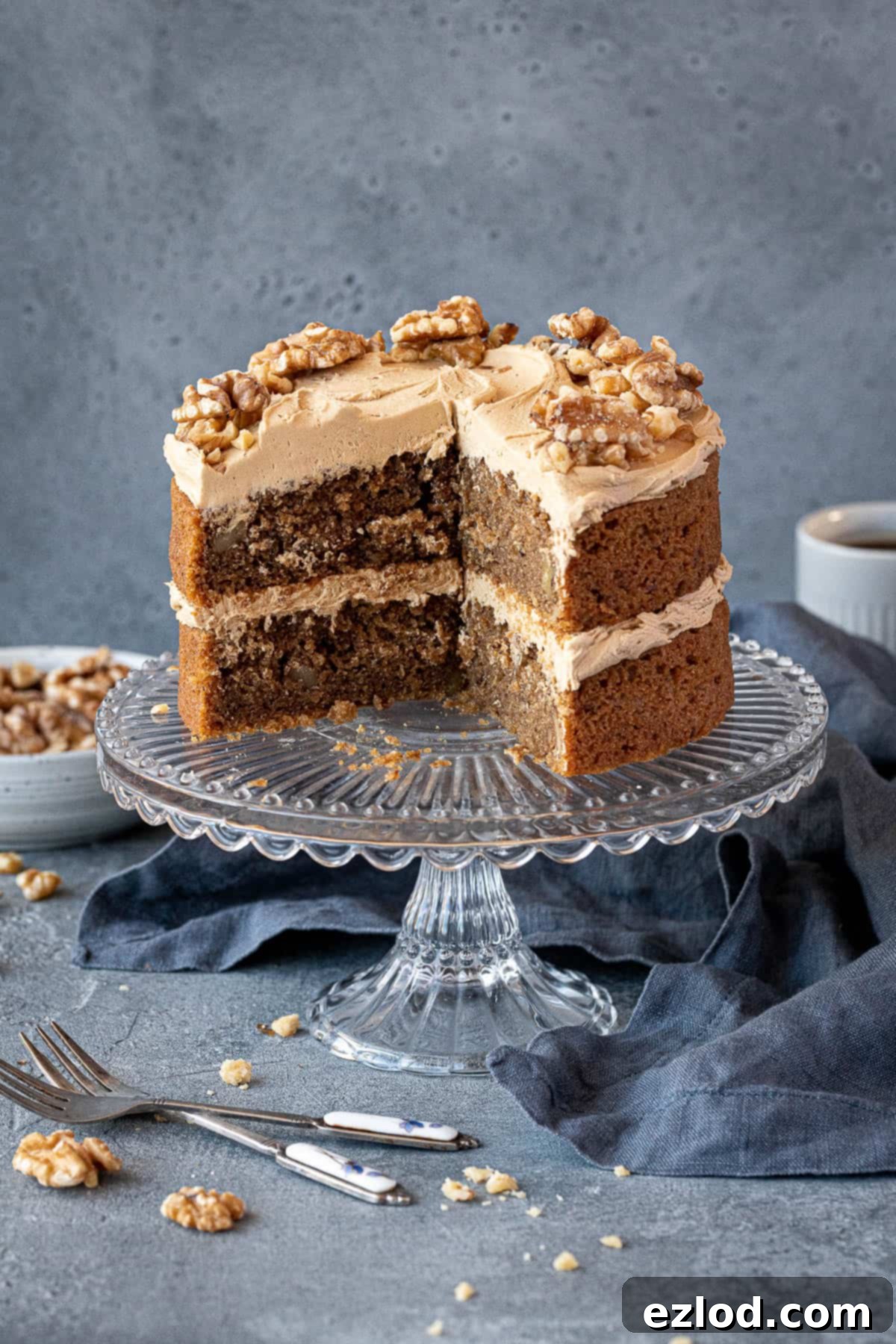 The sliced coffee and walnut cake on a glass cake stand, highlighting the layers of cake and buttercream, and topped with walnuts.