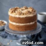 Gluten-free vegan coffee and walnut cake on a glass cake stand with a bowl of walnuts and cups of coffee.