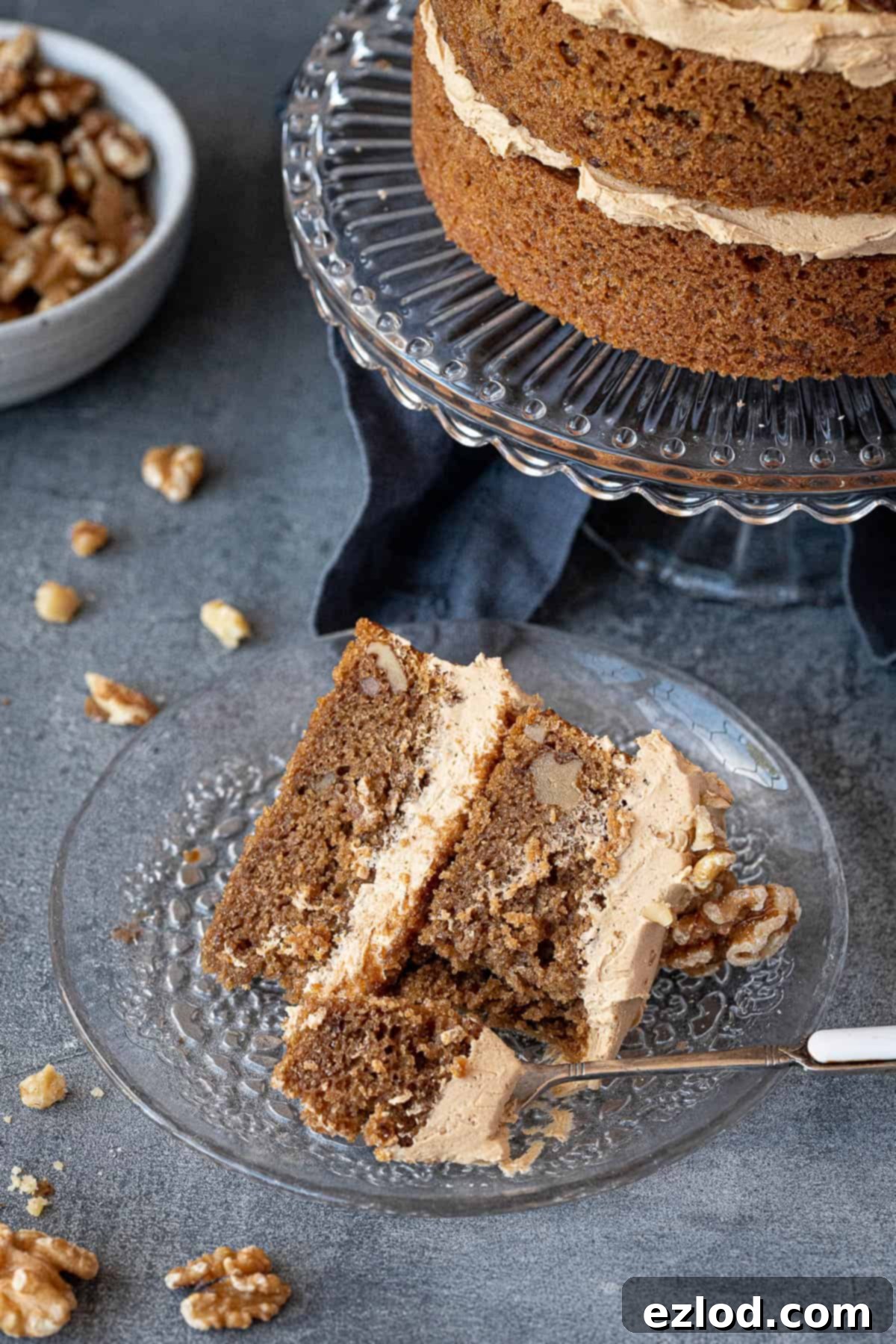 A perfectly cut slice of moist vegan and gluten-free coffee and walnut cake on a glass plate, showcasing its soft texture and creamy frosting.