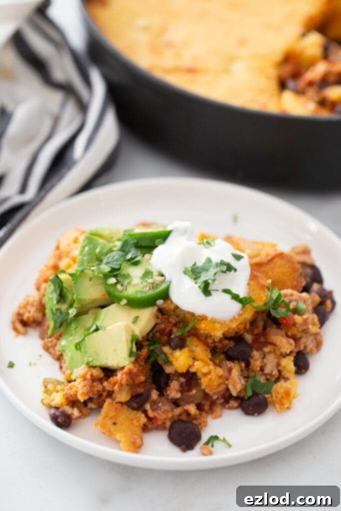 High angle photo of one pan taco chili cornbread topped with avocado, jalapenos, sour cream and cilantro, on a white plate.