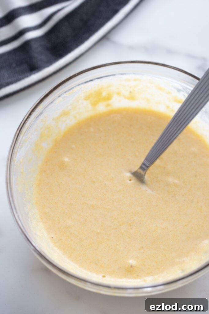 Gluten free cornbread batter in a glass bowl with a utensil.