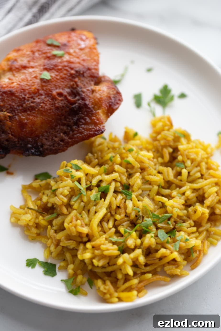 A white plate with homemade Instant Pot Rice a Roni and Air Fryer chicken thighs garnished with fresh parsley.