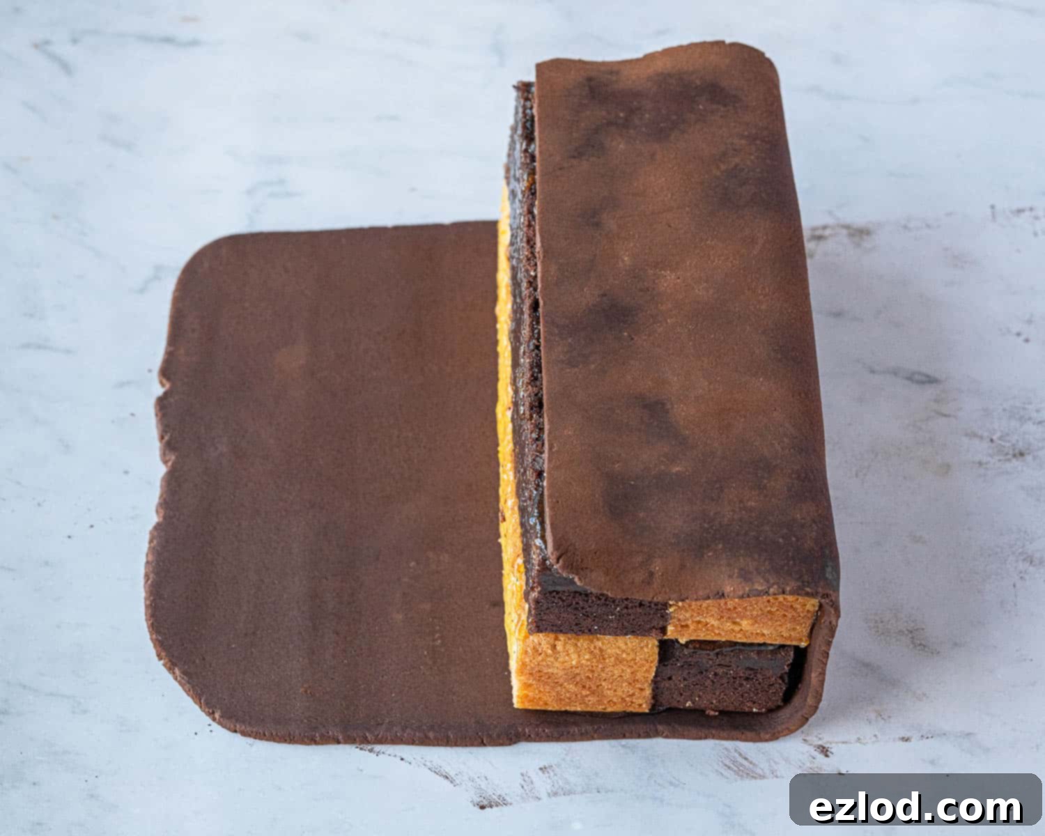 Decadent Vegan Chocolate Orange Battenberg 13 Step 9: Rolling the assembled Battenberg cake block into the marzipan layer, ensuring it is fully encased.