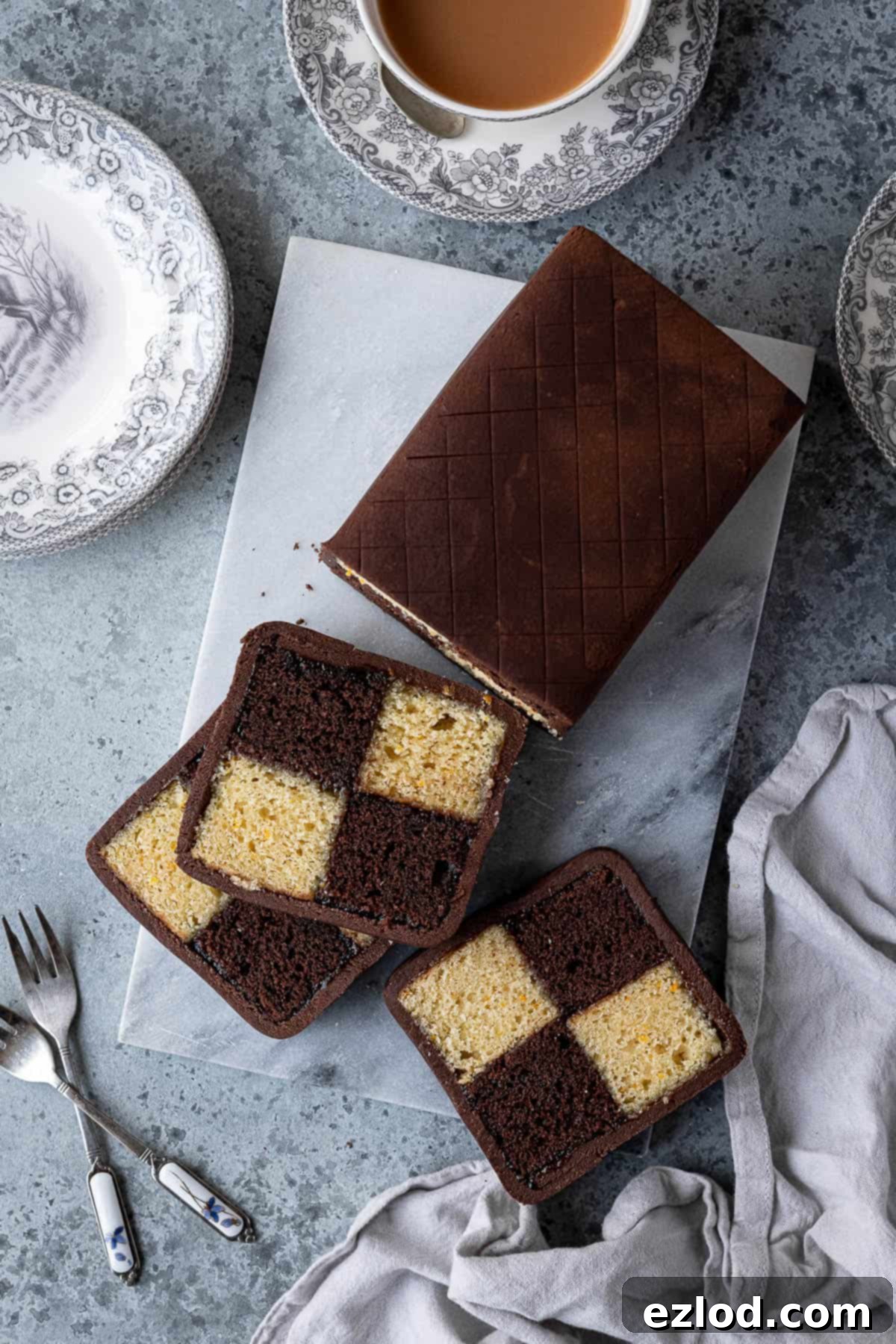 Decadent Vegan Chocolate Orange Battenberg 4 Vegan chocolate orange Battenberg cake on a marble board with plates, forks and a cup of tea, ready to be served.