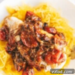 One Skillet Caprese Chicken, topped with melted mozzarella, fresh basil, and a balsamic reduction, served over spaghetti squash in a white bowl.