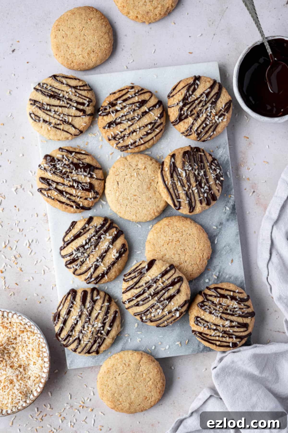 Vegan coconut cookies on a ,marble board with bowls of melted chocolate and toasted coconut.