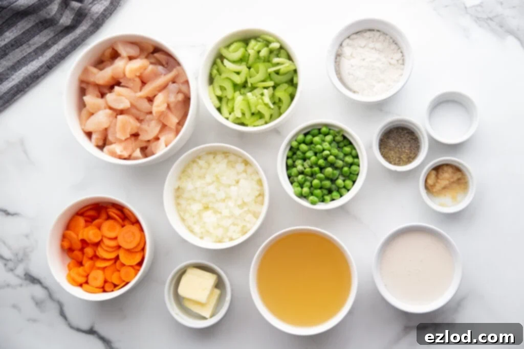 Ingredients for homemade chicken pot pie, including diced chicken, vegetables, and various liquids, arranged in white bowls on a white and grey marble countertop.