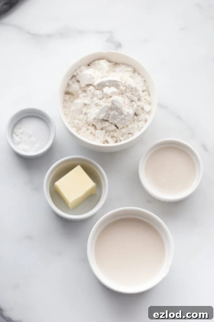 Ingredients for a gluten-free biscuit topping for pot pie, including flour, baking powder, salt, melted butter, and almond milk, laid out on a marble countertop.