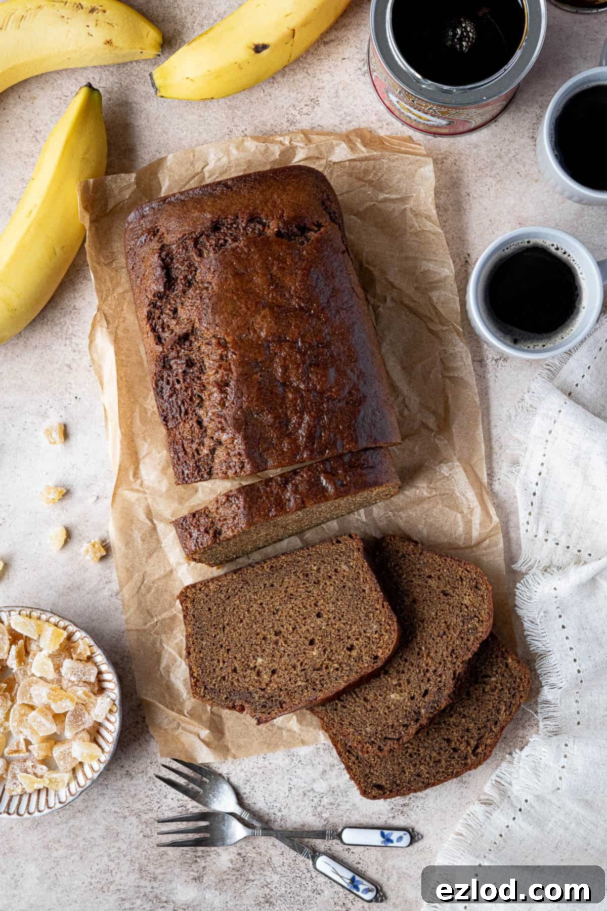 Banana gingerbread with cups of coffee, a tin of treacle, bananas and a bowl of candied ginger.