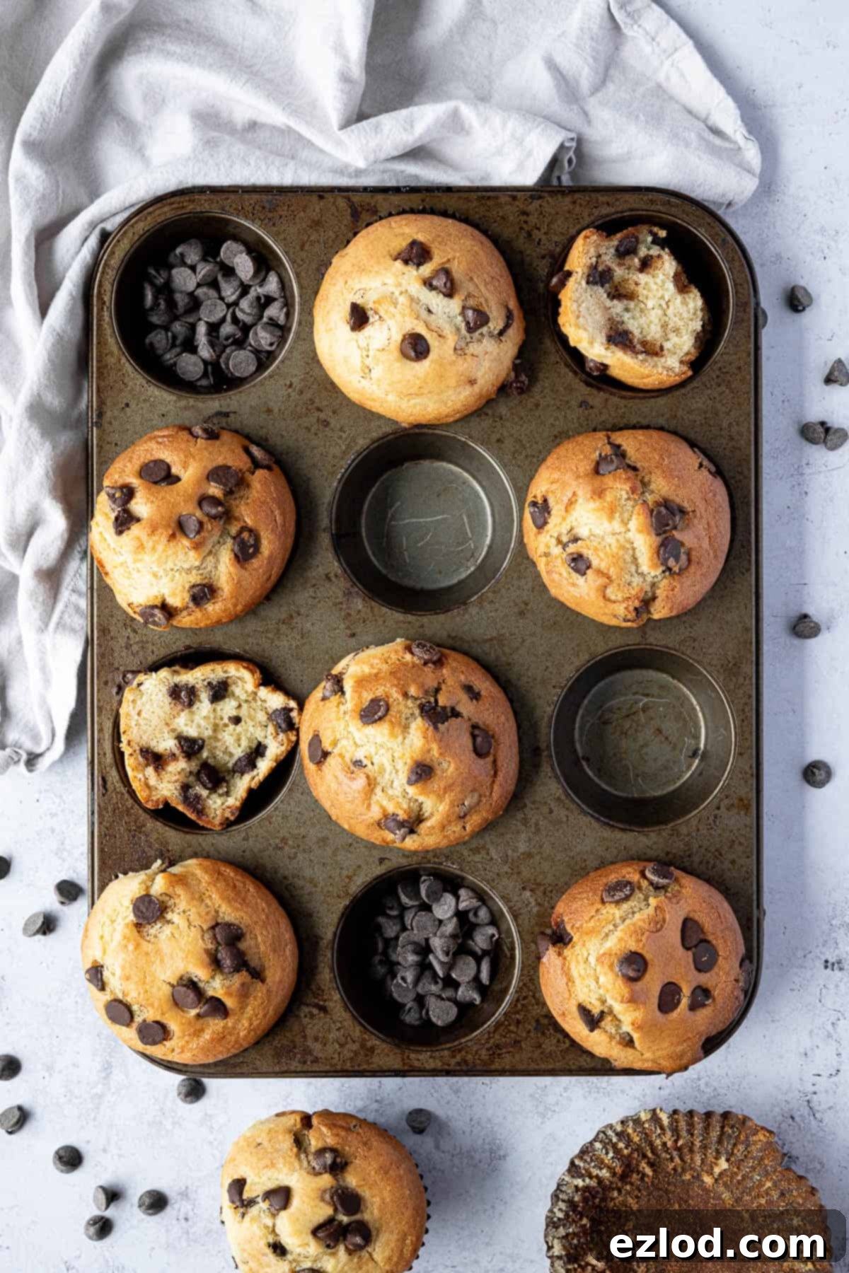 Freshly baked vegan chocolate chip muffins in a muffin tin, overflowing with chocolate chips.