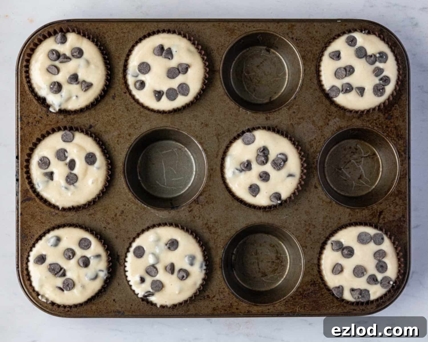 Step 5: Muffin cases filled with vegan chocolate chip batter, topped with extra chocolate chips, ready for baking.