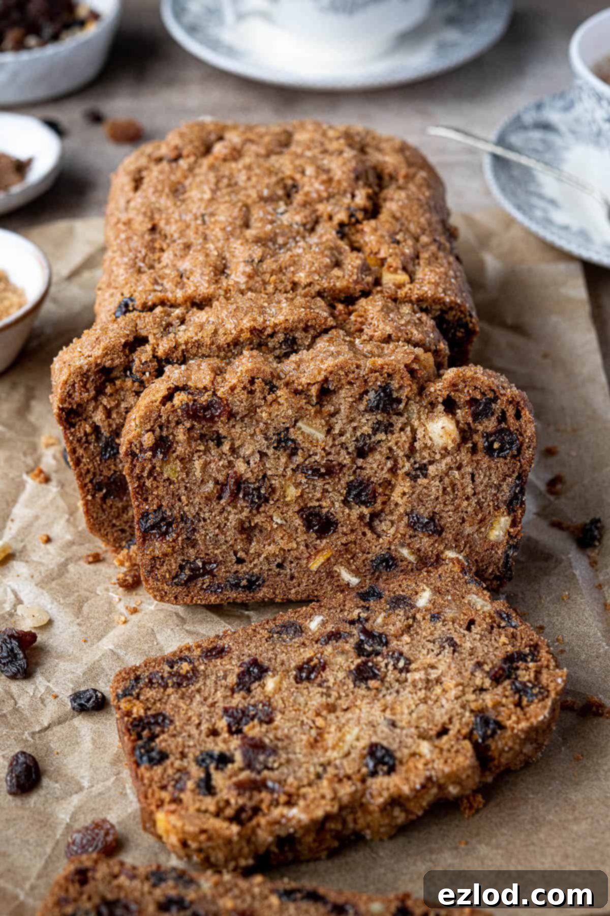 Sliced vegan fruit cake loaf on baking parchment with cups of tea, showcasing its delightful texture and golden crust.