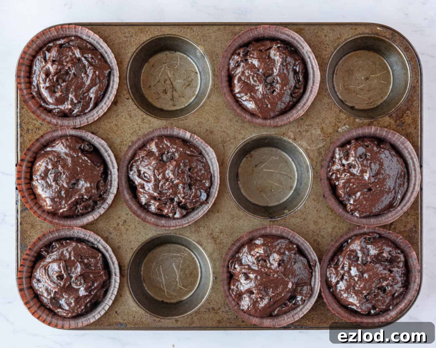Step 5 in making vegan double chocolate muffins: the batter divided evenly between 8 muffin cases, filled to the top.