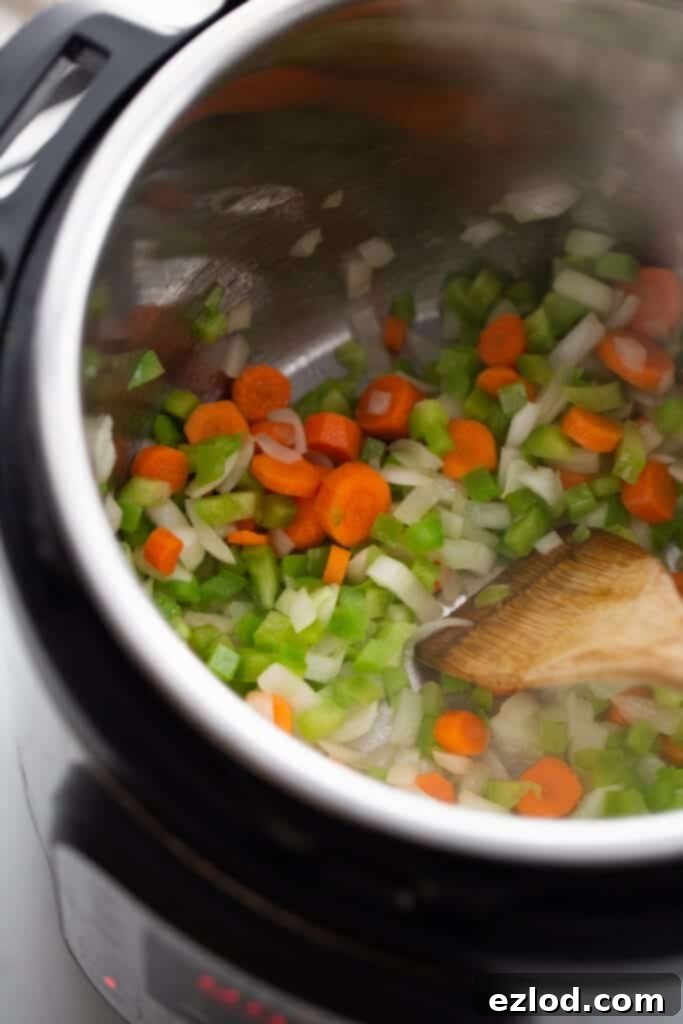 Instant Pot set to sauté with oil, onions, carrots, and bell peppers being cooked.