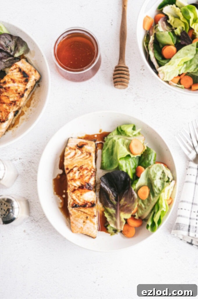 overhead photo of plated grilled salmon dinner on white background with salad, jar of honey and dipping wand