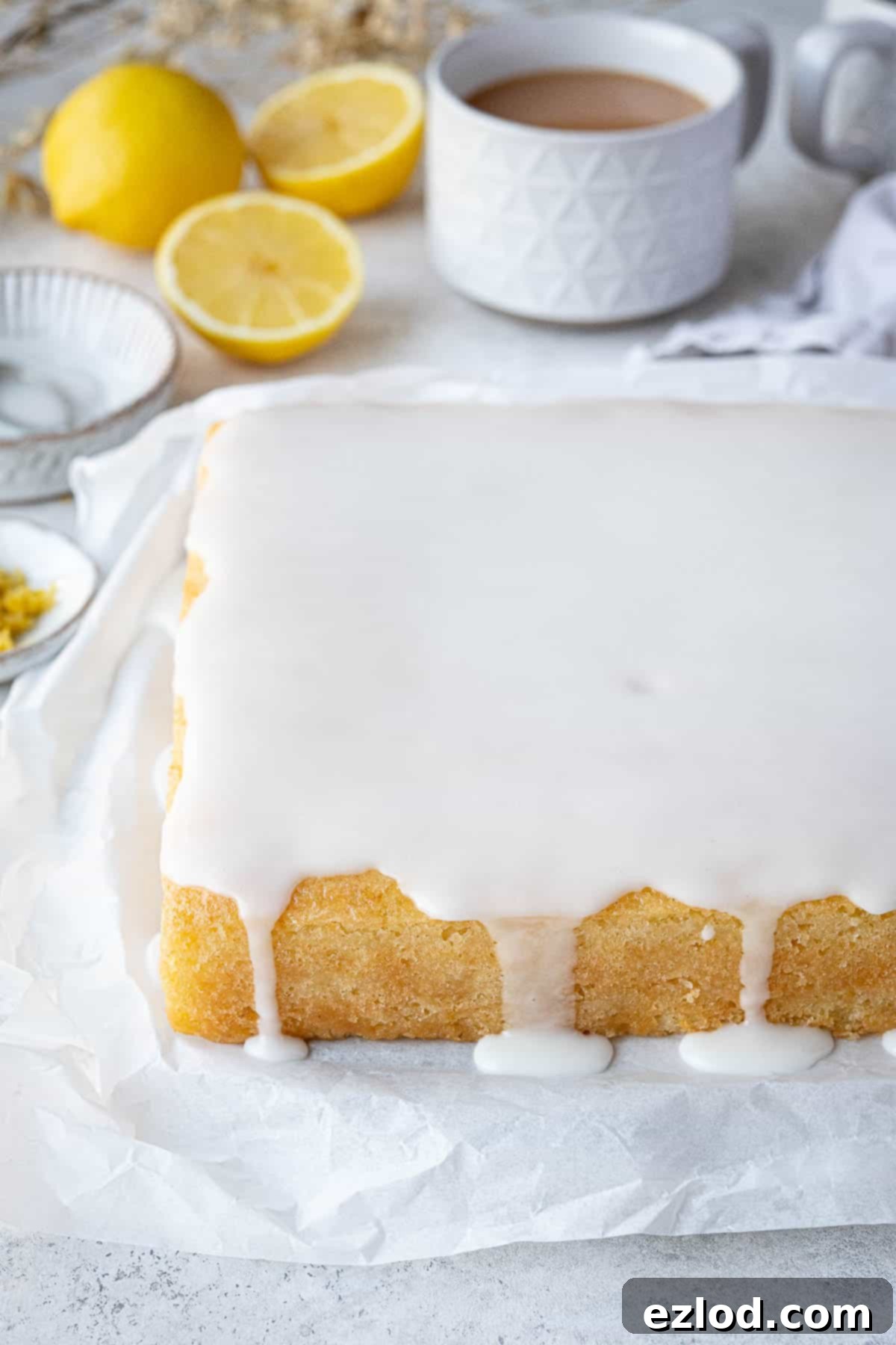 The exquisitely iced gluten-free vegan lemon drizzle cake, presented on a sheet of baking parchment, ready to be sliced and enjoyed.