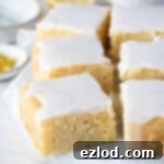 Squares of gluten-free vegan lemon drizzle cake on a sheet of baking parchment with fresh lemons in the background.