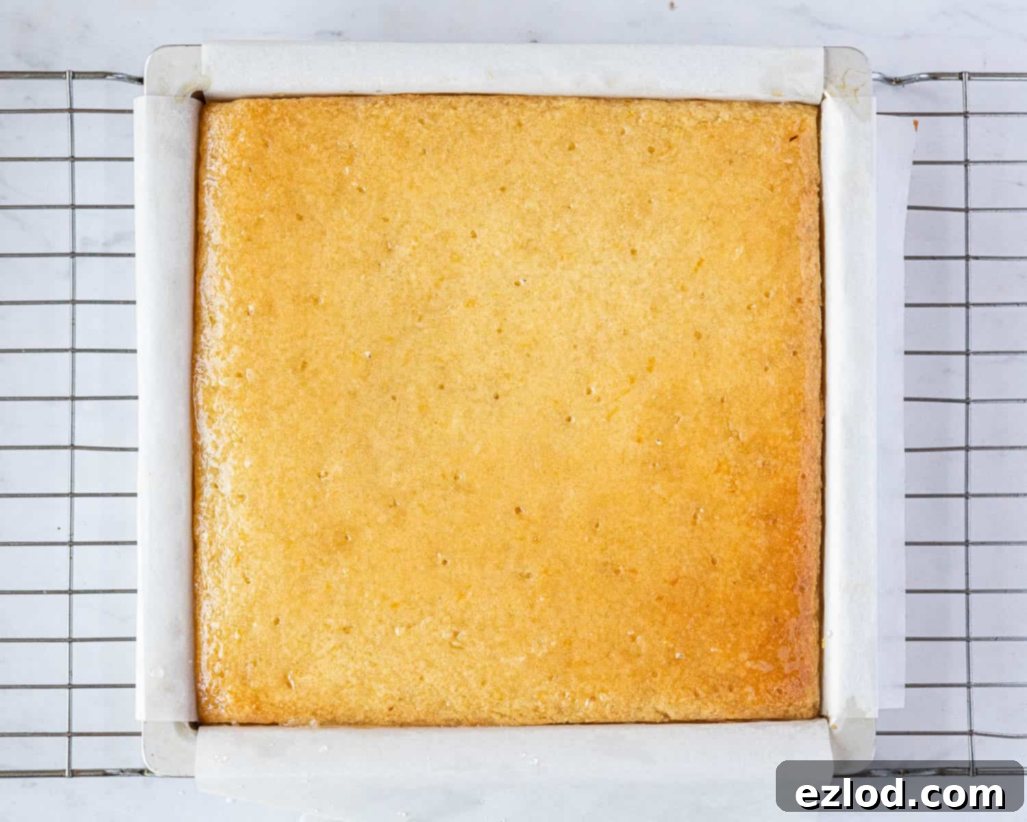 Step 6 in making gluten-free vegan lemon drizzle cake: The warm baked cake, perforated with holes, being generously drizzled with tangy lemon syrup.