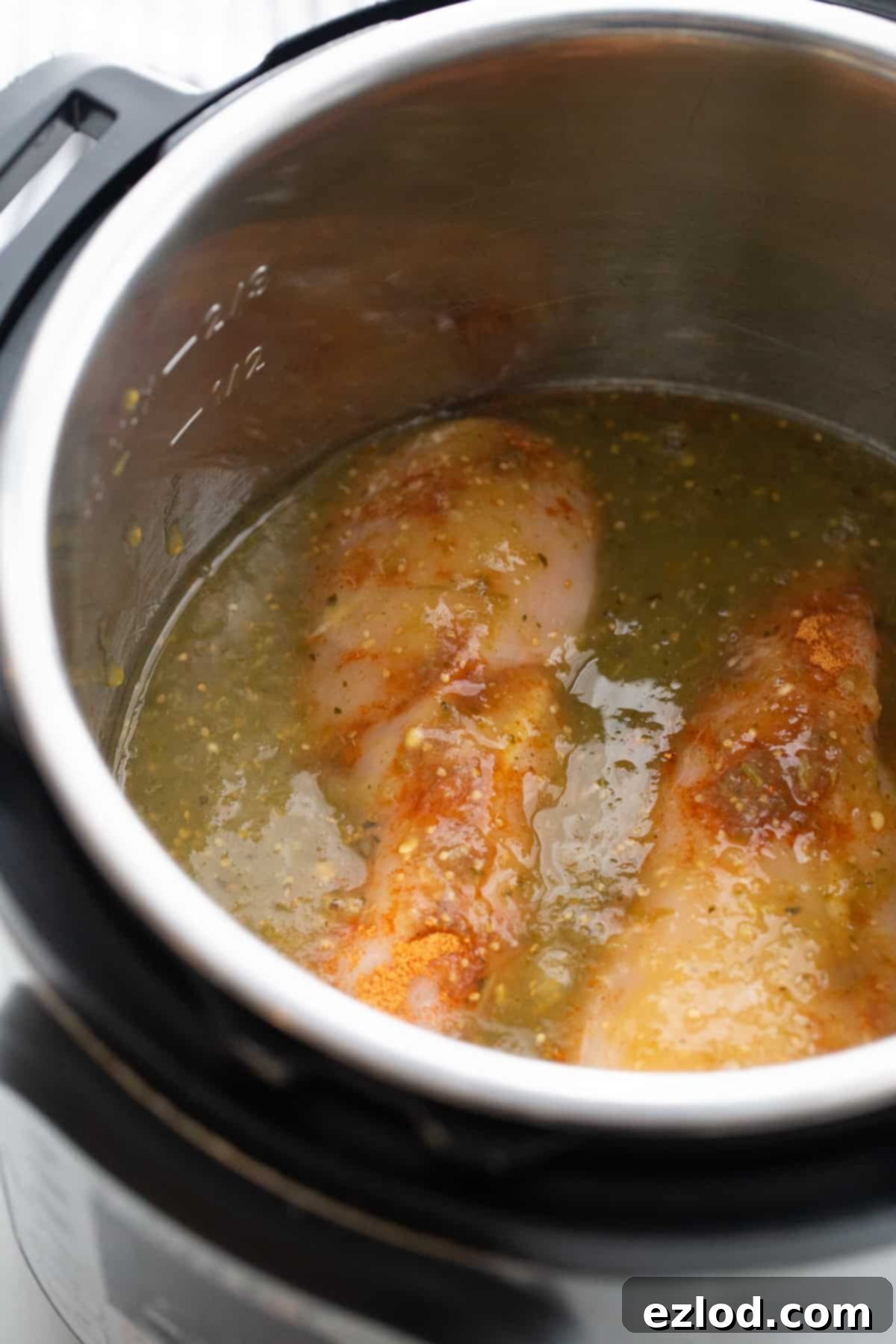 Effortless Salsa Verde Chicken Instant Pot or Slow Cooker 6 Raw chicken and green salsa verde simmering together in an Instant Pot before pressure cooking, showcasing the two main ingredients.