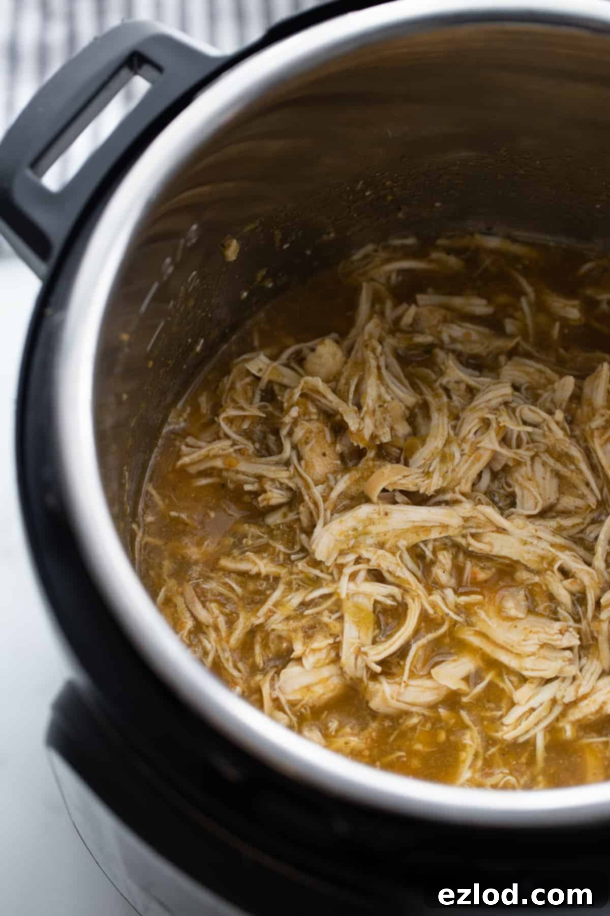 Effortless Salsa Verde Chicken Instant Pot or Slow Cooker 7 A close-up of tender, shredded salsa verde chicken submerged in rich green sauce inside an Instant Pot, ready to be served.