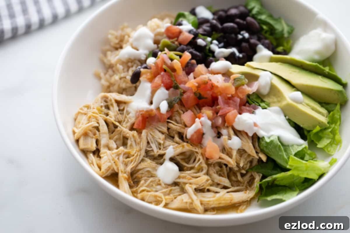 Effortless Salsa Verde Chicken Instant Pot or Slow Cooker 9 A fully loaded burrito bowl featuring shredded salsa lime chicken, adorned with colorful toppings like creamy avocado, fresh pico de gallo, and a generous dollop of Greek yogurt.